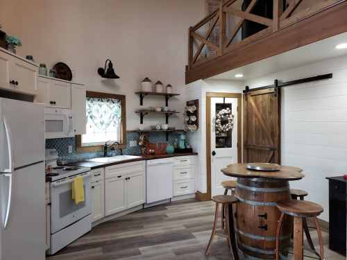 Cozy kitchen with white cabinets, wooden accents, and a round table, featuring a barn door and open shelving.