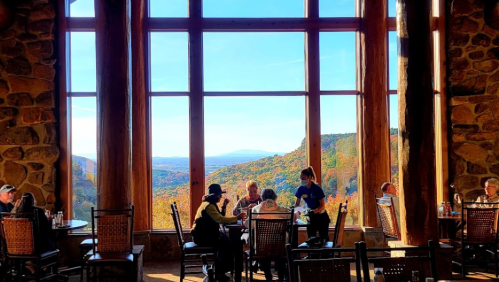 A cozy restaurant with large windows showcasing a scenic mountain view, diners enjoying their meals at wooden tables.