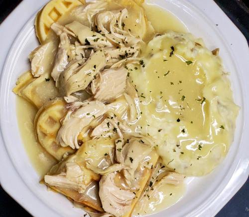 A plate of waffles topped with shredded chicken and gravy, served with a side of mashed potatoes and gravy.