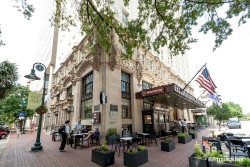 Historic building exterior with outdoor seating, trees, and American flags in a vibrant urban setting.