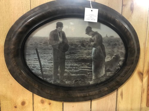 A vintage framed photo of a man and woman in a field, both looking down, with a rustic wooden background.