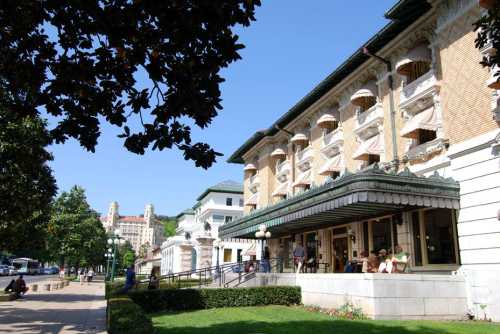 Historic building with ornate architecture, surrounded by greenery and people enjoying the outdoor space.