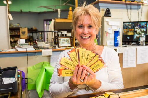 A smiling woman holds several colorful passport tickets at a counter in a shop.