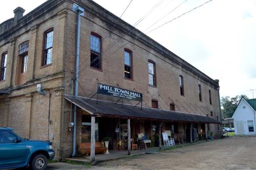 Exterior of Mill Town Mall, a brick building with a sign, featuring outdoor seating and a gravel parking area.