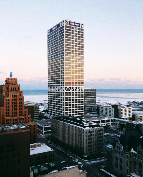 Aerial view of a city skyline featuring a tall bank building and a waterfront in the background during sunset.