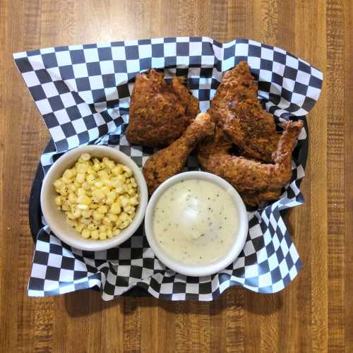 A plate of fried chicken pieces with a side of corn and creamy gravy, served in a checkered basket.