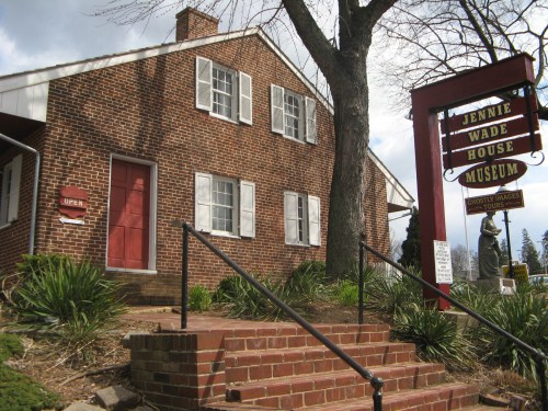 Historic brick house with white shutters, sign for Jennie Wade House Museum, and steps leading up to the entrance.