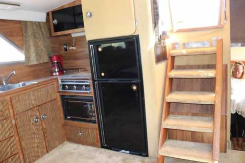 Interior of a boat kitchen featuring a sink, stove, refrigerator, and wooden stairs leading to another area.