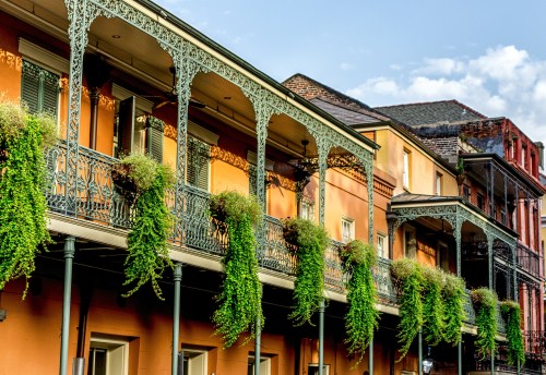 Colorful historic buildings with ornate ironwork balconies adorned with lush green plants under a clear blue sky.
