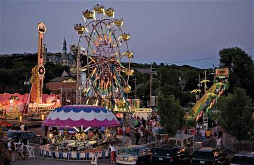 A vibrant carnival scene at dusk, featuring a Ferris wheel, rides, and crowds enjoying the festivities.