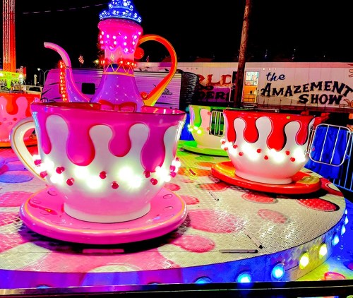 Colorful teacup ride with bright lights, set against a nighttime carnival backdrop.