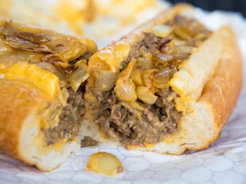 A close-up of a cheesy beef sandwich with sautéed onions on a toasted bun, cut in half to reveal the filling.
