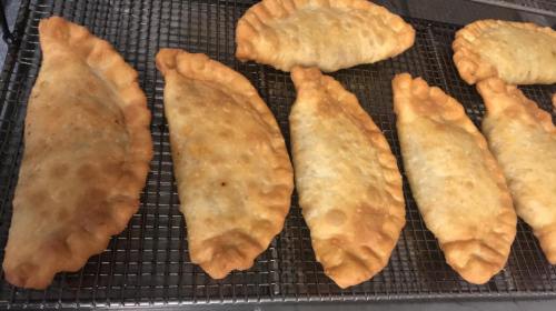 A tray of golden-brown, freshly baked empanadas cooling on a wire rack.