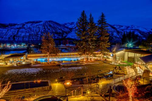 A scenic view of a resort at night, featuring pools, trees, and mountains under a starry sky. Warm lights illuminate the area.
