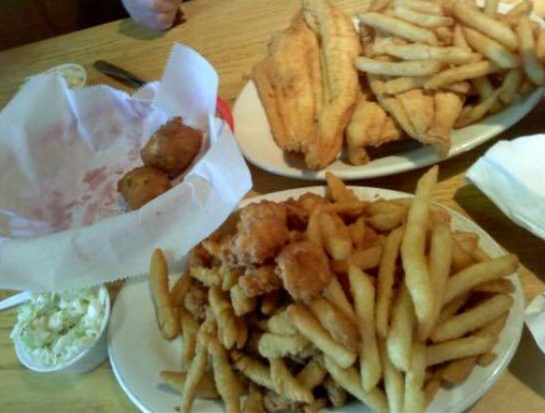 A table with two plates of fried fish and a large serving of French fries, alongside a small bowl of coleslaw.