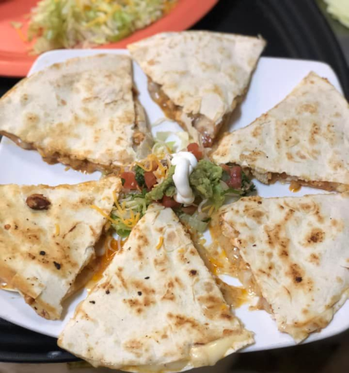 A plate of sliced quesadillas with melted cheese, topped with sour cream, guacamole, and diced tomatoes.