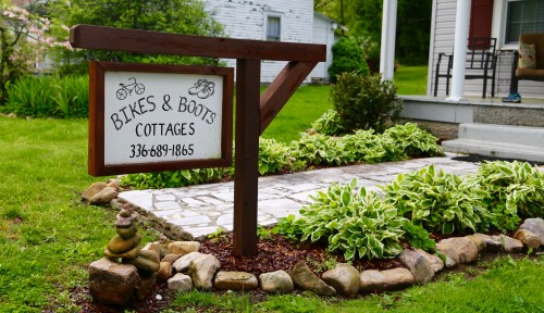 Sign for "Bikes & Boots Cottages" with a stone pathway and lush greenery surrounding it.