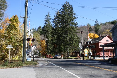 A quiet street scene with a railroad crossing, trees, and colorful autumn foliage in a small town.