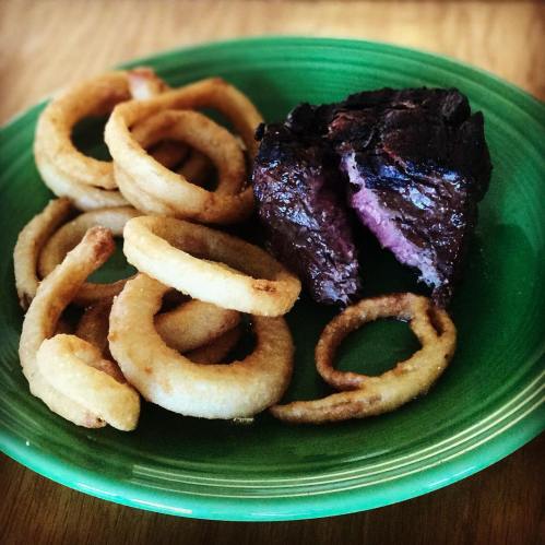 A green plate with a cooked steak and crispy onion rings on the side.