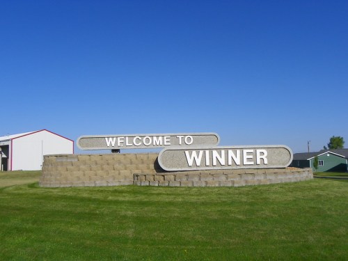 Sign reading "Welcome to Winner" on a grassy area with a clear blue sky in the background.
