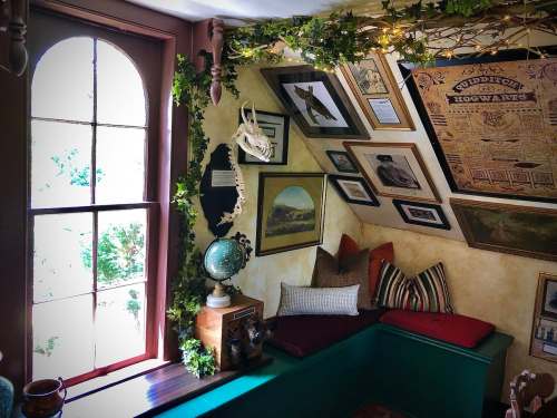 Cozy room with slanted walls, framed art, a globe, and a window surrounded by greenery.