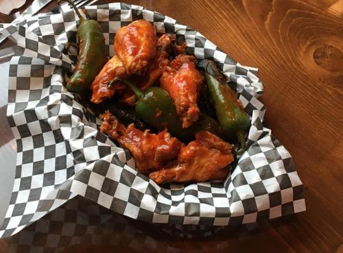 A basket of spicy chicken wings and jalapeño peppers on a checkered paper lining.