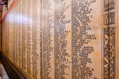 A wall covered in names, likely a memorial or honor roll, with detailed inscriptions on a wooden surface.
