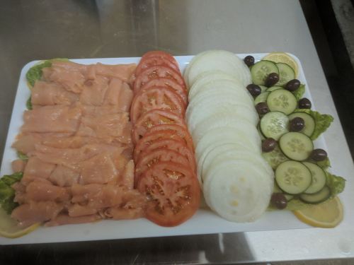A platter with sliced smoked salmon, tomatoes, cucumbers, onions, olives, and lemon on a bed of lettuce.