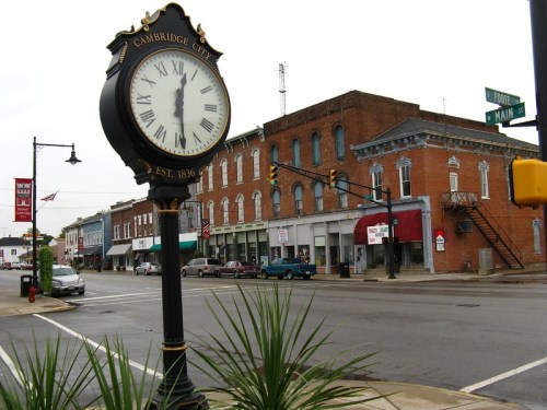 A historic clock stands in front of a quaint street lined with brick buildings in Cambridge City, Indiana.