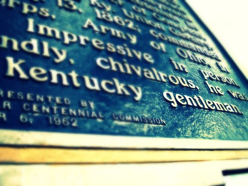 Close-up of a weathered plaque with text about a gentleman from Kentucky, highlighting his chivalrous nature.