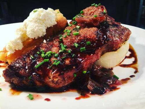 A plated dish featuring steak with a rich sauce, creamy mashed potatoes, and a side of fluffy bread topped with cheese.