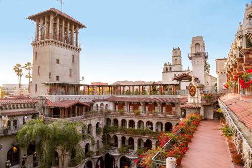 A scenic view of a historic building with a tower, surrounded by lush greenery and vibrant flowers in a courtyard setting.