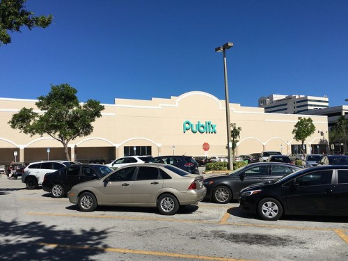 A Publix supermarket with a clear blue sky, surrounded by parked cars in the foreground.