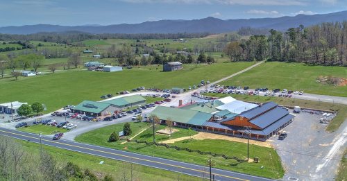 Aerial view of a large building complex with parking, surrounded by green fields and mountains in the background.