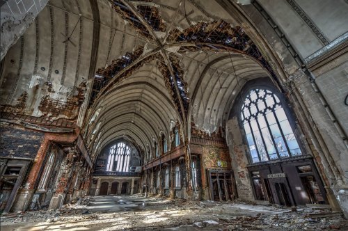 Interior of a dilapidated church with a high, arched ceiling, broken windows, and debris scattered on the floor.