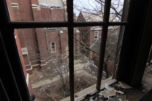 View from a window of an abandoned building, showing overgrown trees and debris in a neglected courtyard.