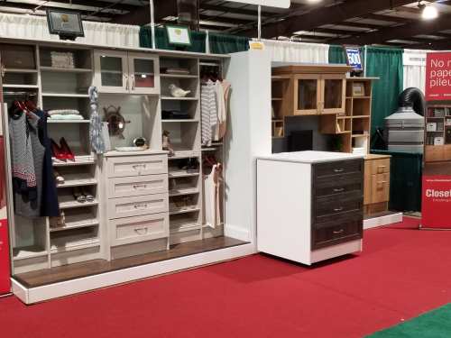 Display of various furniture pieces, including shelving units and dressers, in a trade show setting.