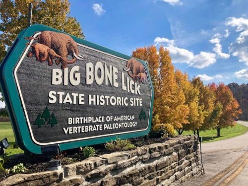 Sign for Big Bone Lick State Historic Site, featuring trees with autumn foliage and a clear blue sky.