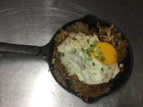 A cast iron skillet filled with crispy hash browns topped with a sunny-side-up egg and green onions.
