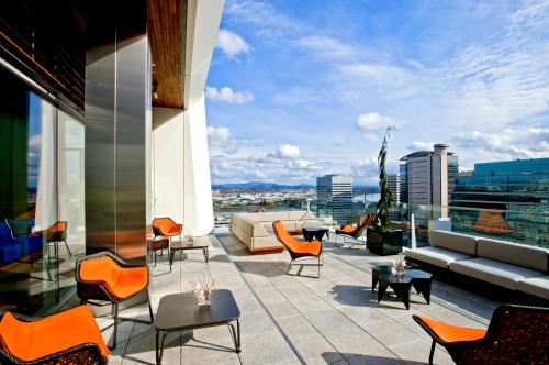 Rooftop terrace with modern furniture, overlooking a cityscape under a blue sky with scattered clouds.