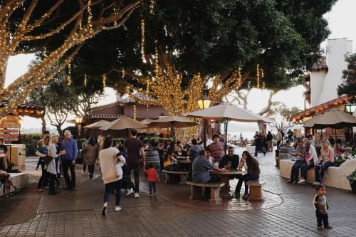 A lively outdoor scene with people socializing under trees adorned with lights, creating a festive atmosphere.