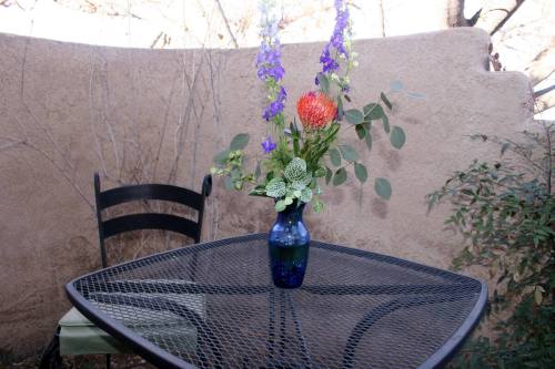 A black metal table with a colorful flower arrangement in a blue vase, set against a textured wall and greenery.