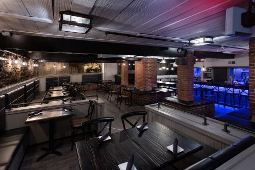 Interior of a modern restaurant featuring dark wood tables, brick columns, and ambient lighting.