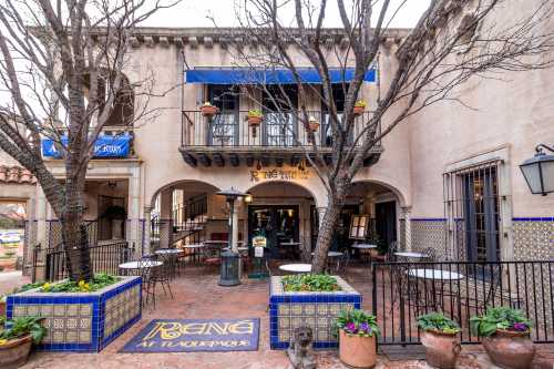 A charming restaurant exterior with a blue awning, potted plants, and outdoor seating in a courtyard setting.