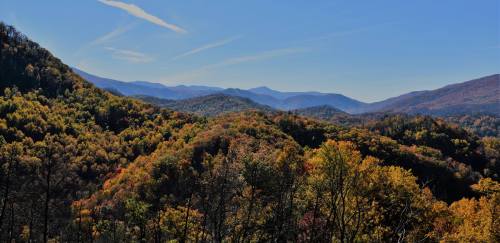A panoramic view of rolling mountains covered in vibrant autumn foliage under a clear blue sky.