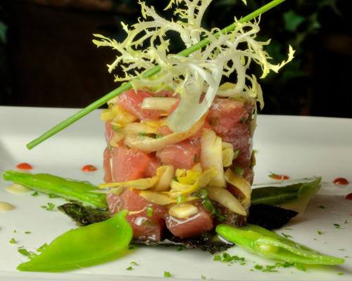A gourmet dish featuring diced tuna, vegetables, and greens, elegantly presented on a white plate with garnishes.