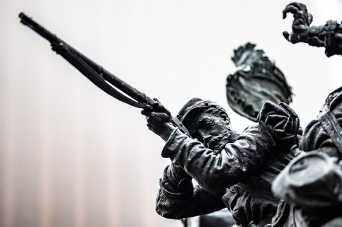 A close-up of a bronze statue depicting a soldier aiming a rifle, showcasing intricate details and expressions.