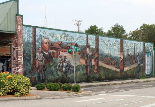 A colorful mural depicting historical scenes with figures in a forest setting, showcasing local culture and heritage.