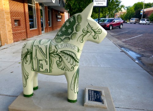 A decorative donkey statue with green designs, including "E Pluribus Unum," on a sidewalk near a library.