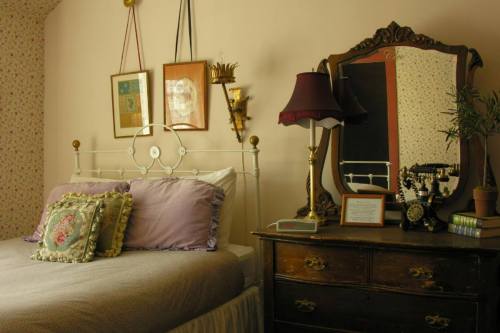 Cozy bedroom with a brass bed, decorative pillows, vintage dresser, and a mirror, featuring soft lighting and floral wallpaper.